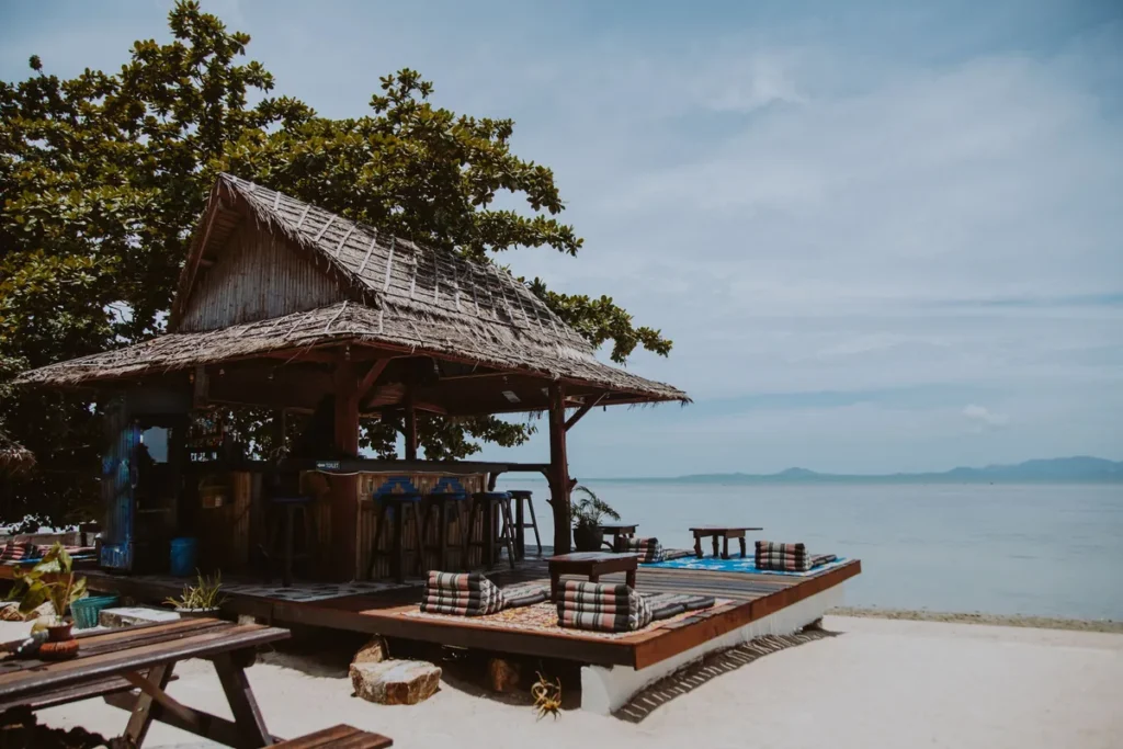 Thatched-roof beach bar with wooden stools and floor cushions on the sand by the sea