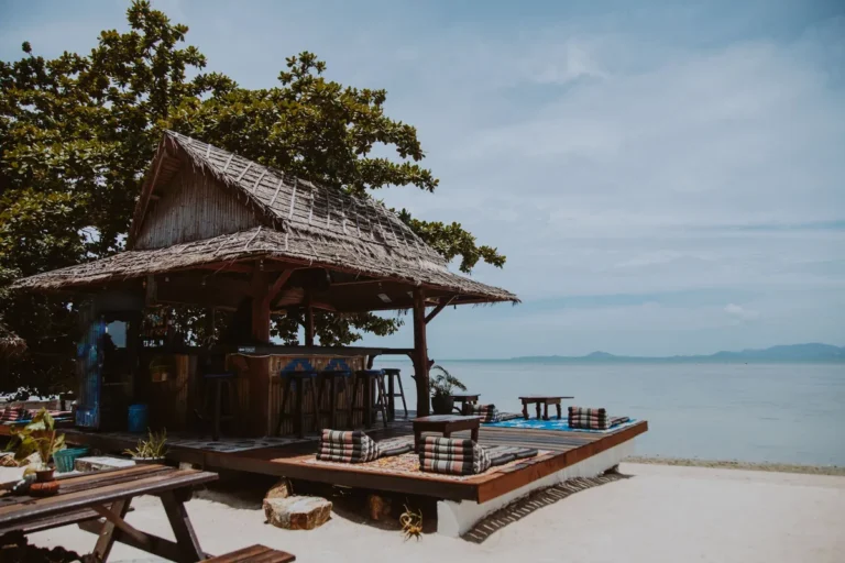 Thatched-roof beach bar with wooden stools and floor cushions on the sand by the sea