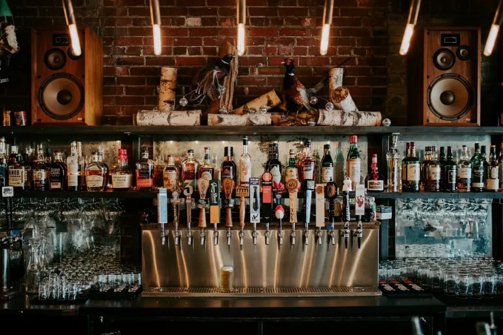 Bar counter with a row of beer taps and shelves of bottles against brick