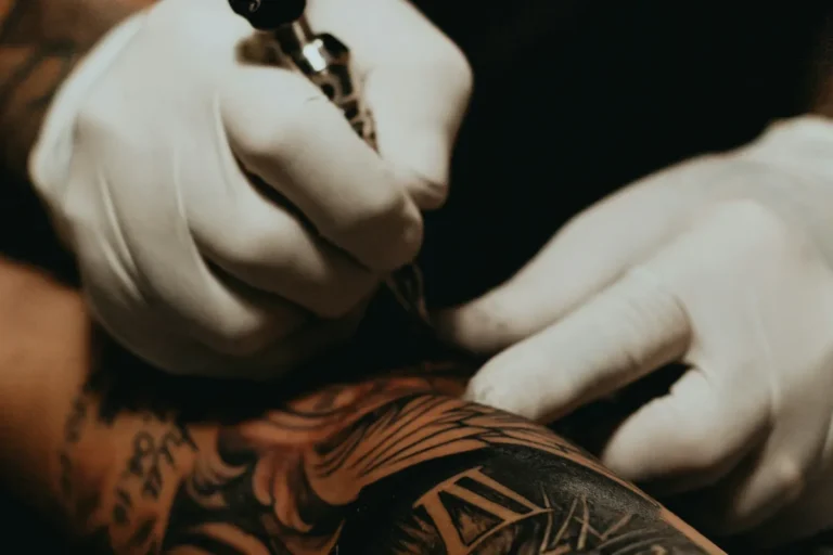 Gloved hands working a tattoo machine on a forearm
