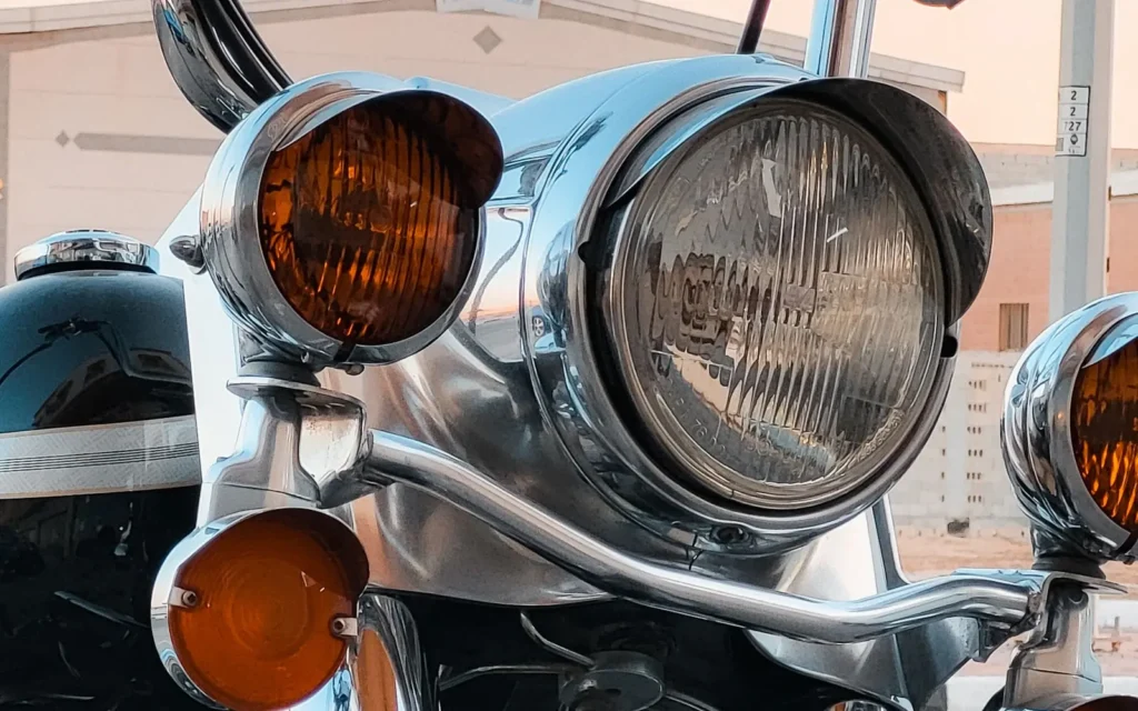 Chrome headlight nacelle, amber passing lamps and handlebars of a touring motorcycle in warm evening light