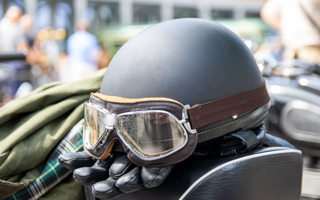 Open-face helmet with leather goggles, riding gloves and a jacket resting on a motorcycle seat
