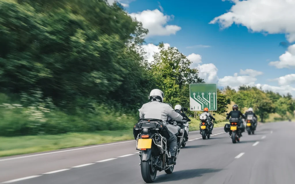 Five touring motorcycles riding in a line down an open two-lane road on a summer day, seen from behind