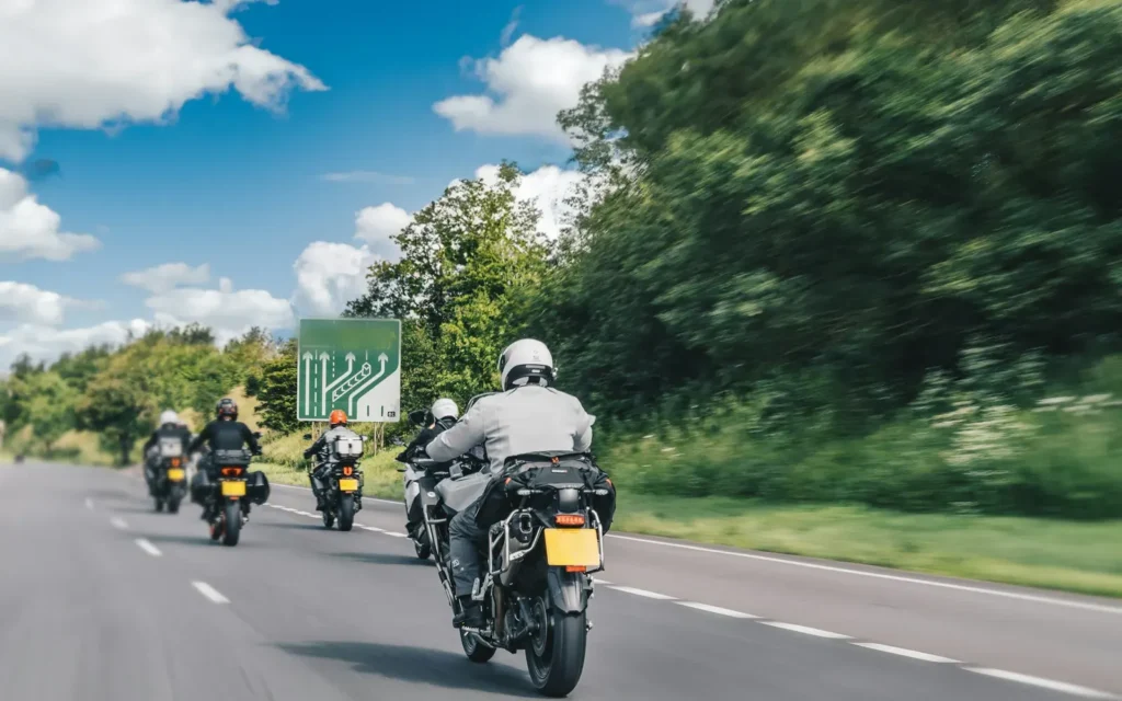 Five touring motorcycles riding in a line down an open two-lane road on a summer day, seen from behind