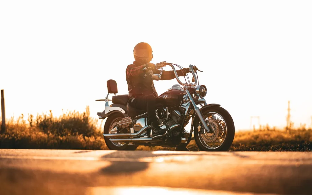 Helmeted rider on a chrome cruiser backlit by golden sunset light on an open road