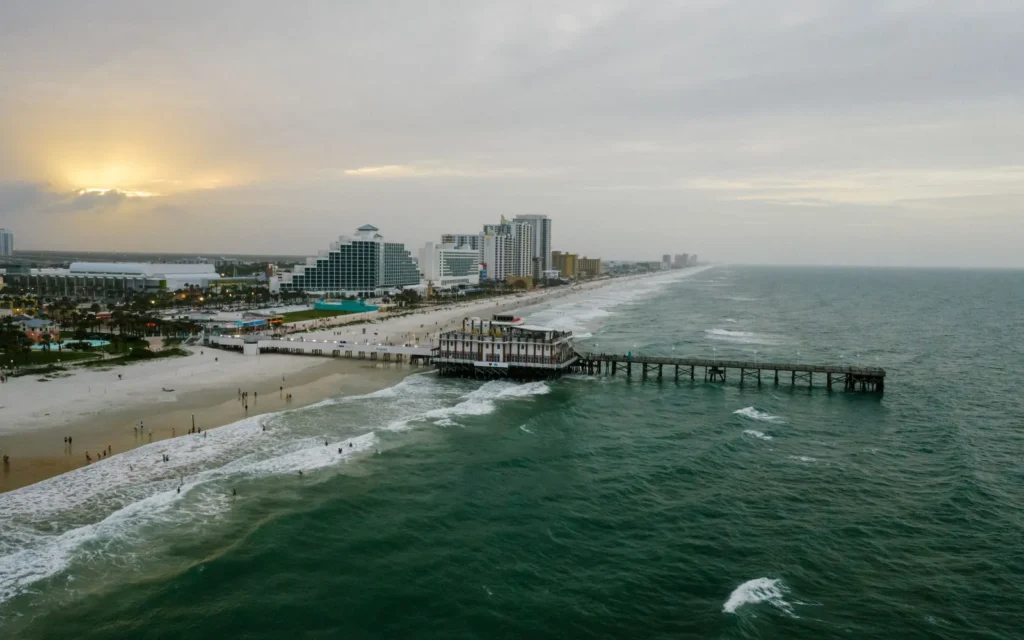 Aerial view of Daytona Beach, FL: the pier, beachfront hotels and green Atlantic surf at sunset