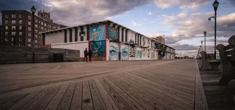 Wide wooden boardwalk with murals under a dramatic sky at the Jersey Shore, the cover photo of our Roar to the Shore guide