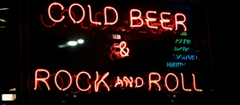 Red neon sign reading Cold Beer and Rock and Roll glowing in a bar window
