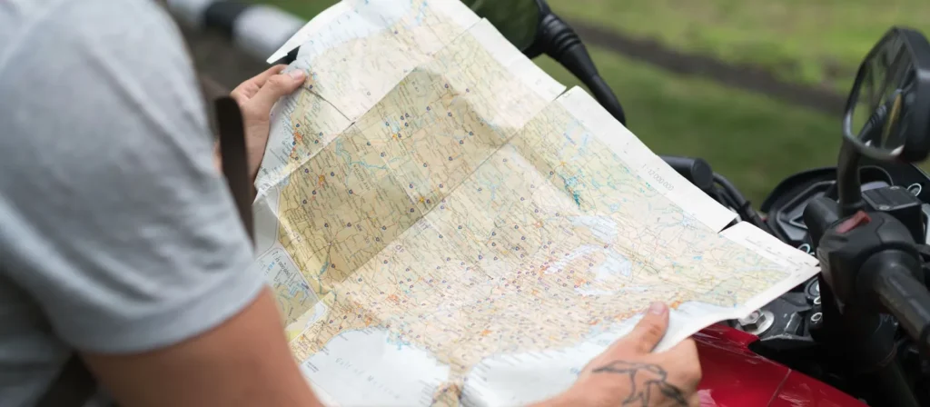 Rider unfolding a road map of the United States over a red motorcycle tank