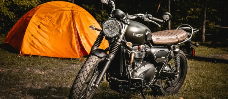 Motorcycle parked beside an orange tent at a wooded campsite