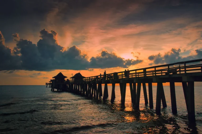 Long wooden fishing pier stretching into the sea under a dramatic sunset sky